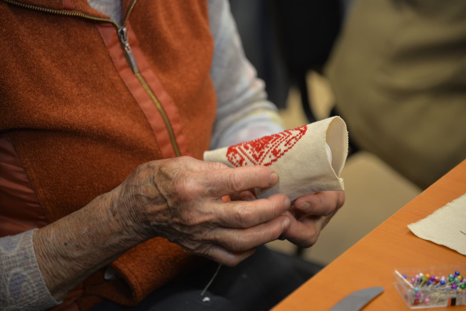 An older maker hand-stitching traditional embroidery at a crafting table