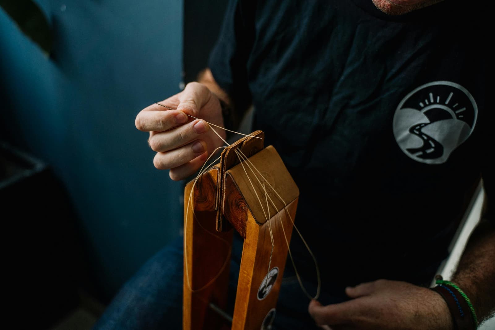Close-up of hands stitching leather with a needle and waxed thread