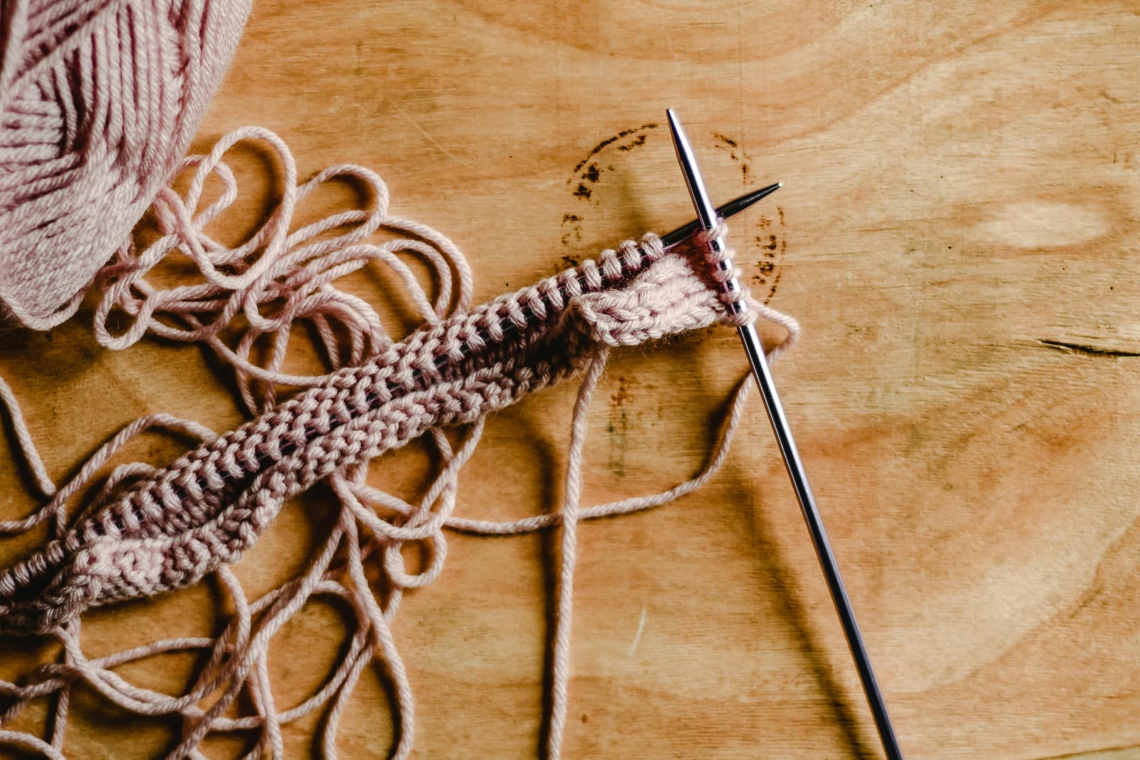 A pair of knitting needles holding stitches of pink wool