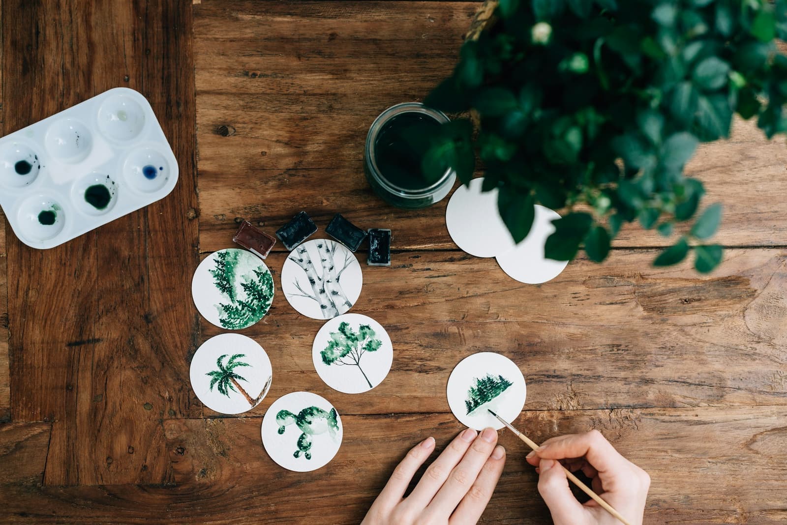 A maker painting botanical designs onto ceramic discs at a wooden workbench